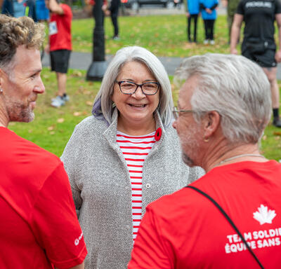 Governor General Mary Simon is speaking with two participants of the Army Run. She is smiling. The photo is taken from behind the two participants.