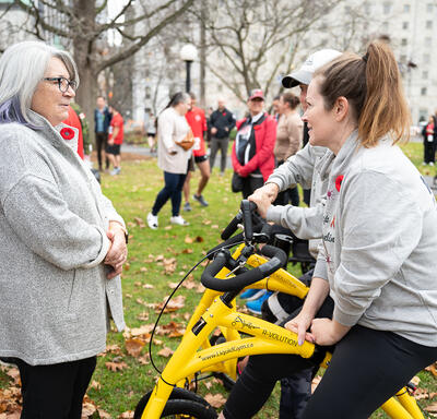 La gouverneure générale Mary Simon parle avec une personne qui est assise sur un petit vélo jaune. Ils sont dans un parc.