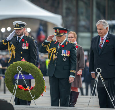 La gouverneure générale Mary Simon salue après avoir déposé une couronne de fleurs sur un trépied au Monument commémoratif de guerre du Canada à Ottawa. Plusieurs personnes sont debout derrière elle.
