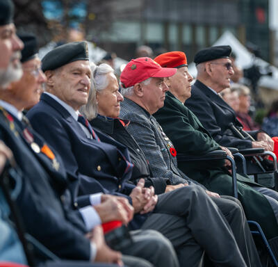 Des gens assis en rangs dehors. Beaucoup d'entre eux portent des uniformes militaires.