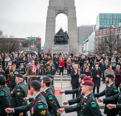 La gouverneure générale Mary Simon salue. Elle porte l’uniforme de l’Armée canadienne. Il y a une foule derrière elle. Des membres des Forces armées canadiennes marchent devant elle et la regardent.