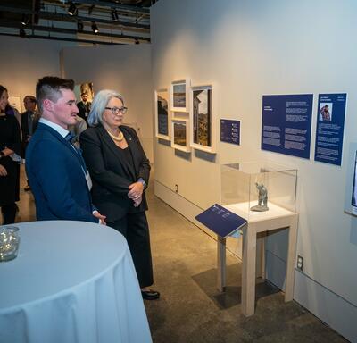 The Governor General is looking at a tv screen that is part of the exhibit.