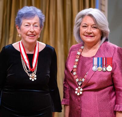 La gouverneure générale Simon se tient à côté d’une femme qui porte une médaille autour du cou.