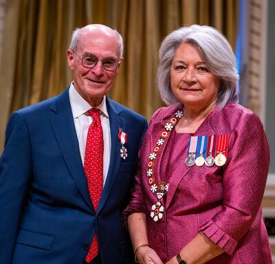 Governor General Simon is standing next to a man who has a medal pinned to his blue blazer.