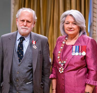 Governor General Simon is standing next to a man who has a medal pinned to his grey blazer.