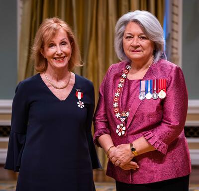 La gouverneure générale Simon se tient à côté d’une femme qui porte une médaille épinglée à sa robe bleue.