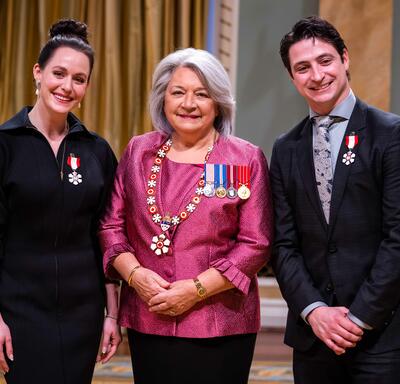 Governor General Simon is standing between a man and a woman who have medals pinned to their shirt and blazer..
