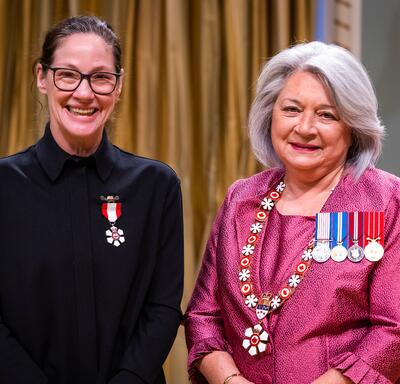 La gouverneure générale Simon se tient à côté d’une femme qui porte une médaille épinglée à sa chemise noire.