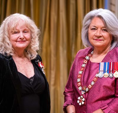 La gouverneure générale Simon se tient à côté d’une femme qui porte une médaille épinglée à son blazer noir.