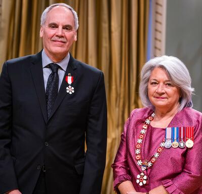 Governor General Simon is standing next to a man who has a medal pinned to his black blazer.