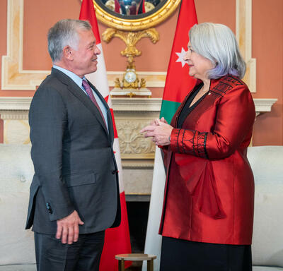 Governor General Mary Simon, wearing a red vest, is facing and talking to the King of Jordan, wearing a grey vest and purple tie. 