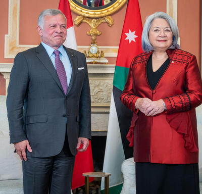 Governor General Mary Simon, wearing a red vest, is standing next to the King of Jordan, wearing a grey vest and purple tie. 