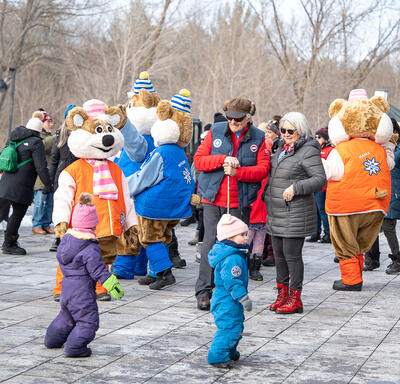 Governor General Simon and Mr. Fraser are smiling at a group of children. The Winterlude Ice Hogs and a group of people stand behind them.