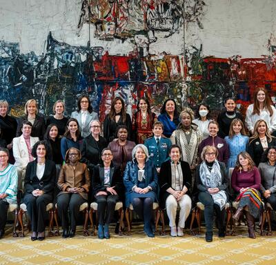 A group of approximately 40 women pose with Governor General Simon for a photo in the Ballroom at Rideau Hall. They are gathered in front of a large painting.