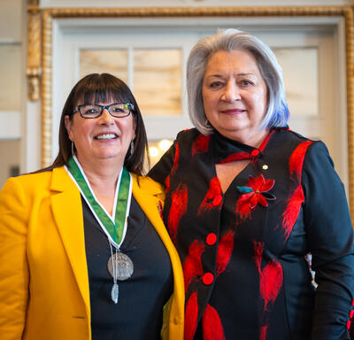 Governor General Simon stands next to a woman wearing a medal around her neck. Both of them are smiling. 