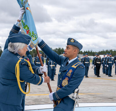 Governor General Mary Simon holds the colours and hands it over to a member of the Canadian Armed Forces