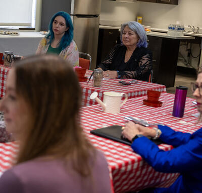 Un groupe de personnes est assis attentivement autour d'une table recouverte d'une nappe à carreaux rouges dans une cuisine.