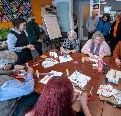 La gouverneure générale Mary Simon assise à une table avec un groupe de personnes. Certaines sont assises, d'autres sont debout. Plusieurs articles de bricolage sont posés sur la table.