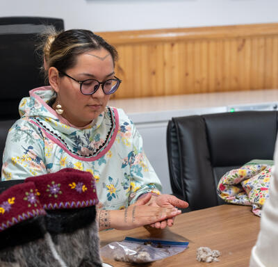 Une femme assise à une table. Elle tient quelque chose entre ses mains.