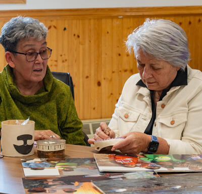 La gouverneure générale Mary Simon en train de coudre quelque chose. Elle est assise à une table avec une autre personne.