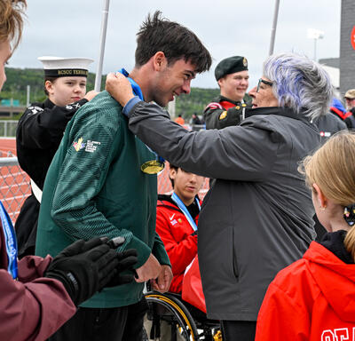 Governor General Mary Simon placing a medal around an athlete's neck. 