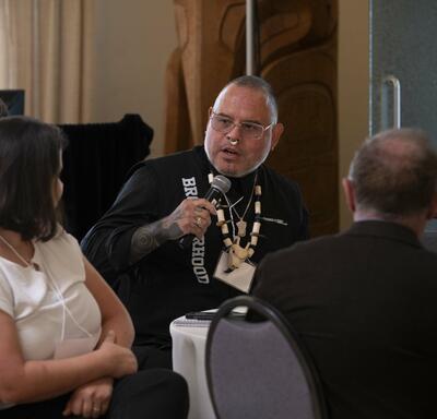 Des personnes assises à une table. Une personne tient un micro.