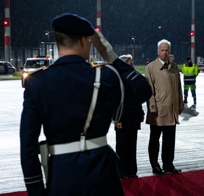 A man in uniform is saluting an official from the German govermment. They are outside standing on the red carpet on the tarmac at the airport.