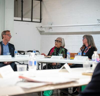 Un groupe de personnes est assis autour d'une table de conférence et discute. Des documents et des bouteilles d'eau sont posés sur la table.