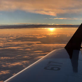 View of airplane wing from inside a plane with the sun setting.