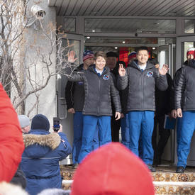 Anne McClain, Oleg Kononenko and David Saint-Jacques stand outside, side by side, at the top of a short stair case and wave at the crowd.