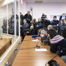 David Saint-Jacques is seated in front of a microphone.  He is separated from the crowd by large glass windows.  The crowd is composed of Governor General, Julie Payette, family members and media.
