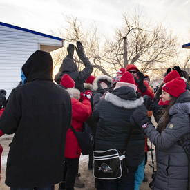 A crowd wearing Canadian tuques and mitts celebrate and look towards the sky. 