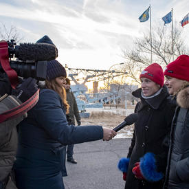 The Governor General, Julie Payette, and Véronique Morin, spouse of astronaut David Saint-Jacques are being interviewed.   A female journalist hold a microphone towards them while they are filmed by a large hand held camera. 