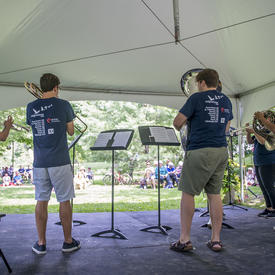A picture taken from behind a troupe of musicians as they play for an audience on the grounds of Rideau Hall.