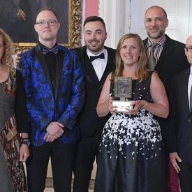 A group of 5 people representing the Telegraph-Journal are posing with Governor General Julie Payette who is at the extreme left. A lady in the middle is holding the Michener Award trophy.