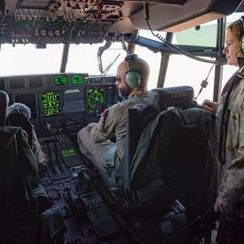 Governor General Julie Payette watches a pilot and his co-pilot at work in an aircraft cockpit.