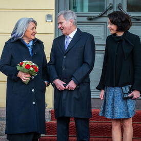 Holding a bouquet of flowers, Governor General Simon stands next to President Sauli Niinistö and his spouse, Dr. Jenni Haukio.