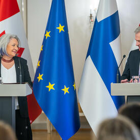 Governor General Simon and President Sauli Niinistö are standing at a podium. Behind them, in order from left to right, are the flags of Canada, Finland and the European Union.  