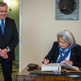 La gouverneure générale Mary Simon signant un livre des visiteurs. Le premier vice-président, Antti Rinne, est debout à sa droite.