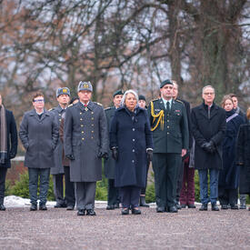 La gouverneure générale Mary Simon se tient devant un groupe de personnes sur une route de gravier. Leurs expressions sont sombres. Plusieurs personnes portent un uniforme militaire.
