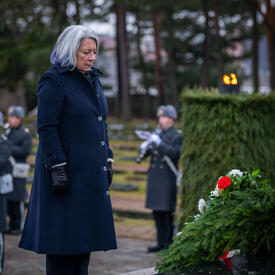 La gouverneure générale Mary Simon se tient devant une couronne de fleurs déposée sur un monument noir. Une fanfare militaire joue derrière elle.