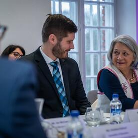 Governor General Simon sitting at a large table, smiling to a man on her right.  La gouverneure générale Mary Simon, assise à une grande table, sourit à un homme assis à sa droite.