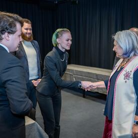 La gouverneure générale Mary Simon serre la main d’une jeune femme. Quatre autres jeunes gens se tiennent à proximité et les regardent.