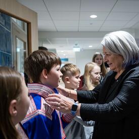 La gouverneure générale Mary Simon parle à un élève, les mains posées sur ses épaules. D’autres étudiants l’entourent et un homme se tient derrière elle.