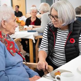 The Governor General chats with a woman. They are seated at a dining table.