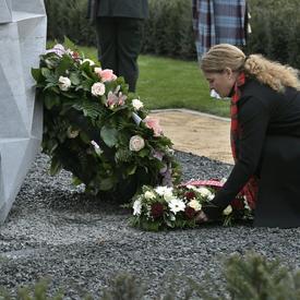 The Governor General of Canada is laying a wreath of flower on a tomb in a cemetary.