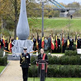 La gouverneure générale du Canada prend la parole à une tribune, avec sa femme aide-de-camp à sa droite. Derrière elle se trouve une sculpture géante en béton en forme de larme.