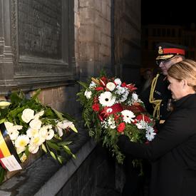 La gouverneure générale du Canada dépose une gerbe de fleurs devant un monument mural la nuit avec l'aide d'un militaire.