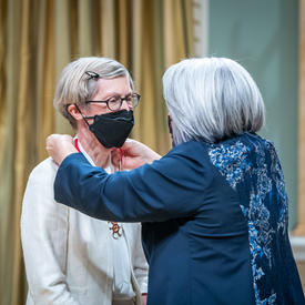 The Governor General is placing a medal around Robin McLeod’s neck.