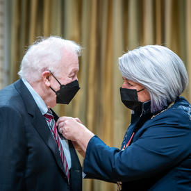 The Governor General is placing a pin on Joseph Raymond Buncic’s suit jacket.